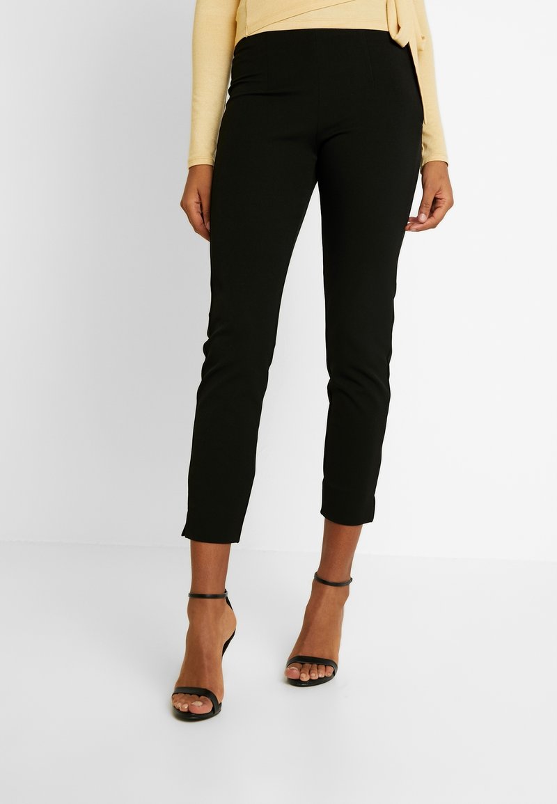 Svarta cropped byxor med smal passform, med en slät yta och elastisk midja. Bärs med svarta sandaletter och en gul topp.