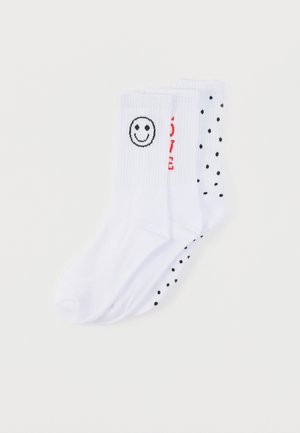 Chaussettes en coton blanc avec un visage souriant sur une chaussette et des pois noirs sur l'autre, avec un texte rouge indiquant "LOVE" sur le côté.