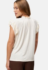 Crème korte mouwen top met gerimpelde accenten op de schouders, met een losse pasvorm en een geweven stof, bekeken vanuit de achterkant.