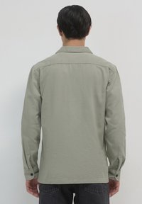 Camicia verde chiaro con maniche lunghe, tessuto uniforme e colletto. Presenta polsini con bottone e orlo dritto. Vista posteriore.