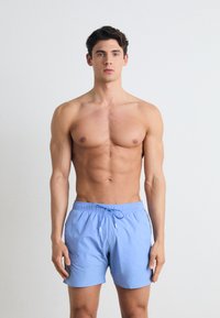 Shorts de bain bleu clair avec une taille élastique et un cordon de serrage, fabriqués en tissu lisse, dotés de poches latérales et d'une coupe décontractée.