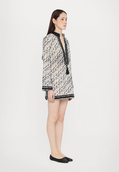 Tunic cu model alb și negru, cu decolteu în V și detalii cu ciucuri, având mâneci lungi și bordură contrastantă la marginea de jos și la manșete.