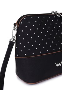 Black leather handbag featuring white polka dots, a smooth texture, bronze accents, and a silver logo. Includes a detachable strap.