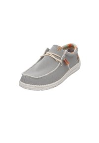Zapatilla de lona gris con suela de goma blanca, parte superior texturizada, costuras a tono y cordones beige. Forro interior con un patrón colorido visible.