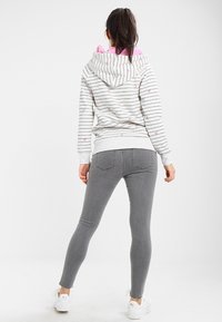 Sudadera gris a rayas con interior rosa, que presenta pequeños patrones de corazones. Combinada con jeans ajustados grises y zapatillas blancas.
