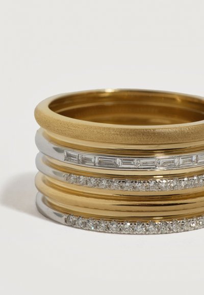 Zloženi zlati in srebrni prstani, nekateri z jasnimi pravokotnimi in okroglimi diamanti, na belem ozadju.