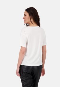 Weißes kurzärmeliges T-Shirt mit Rundhalsausschnitt, aus weichem Baumwollmaterial, von hinten gezeigt, kombiniert mit schwarzen Kunstlederhosen.