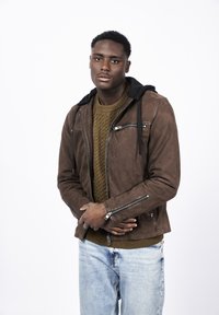 Brun mockaskinnjacka med dragkedjefickor, svart huva och en texturerad olivgrön tröja under; i kombination med ljusblå jeans.