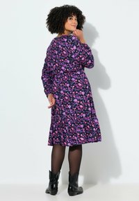 Sukienka w kwiatowy wzór w odcieniach fioletu i różu na czarnym tle, z długimi rękawami, falbaną u dołu, zestawiona z czarnymi botkami za kostkę.