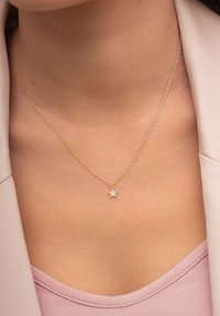Goldene Halskette mit einem sternförmigen Anhänger und einem zentralen Edelstein. Glatte Oberfläche, feine Gliederkette und elegantes Design.