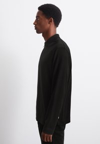 Black long-sleeve polo made of smooth fabric, featuring a collared design and a straight cut. Subtle accents near the hem.