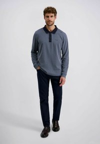 Marineblaues Langarm-Polohemd mit strukturiertem Strickmuster, ausgestattet mit einem dunklen Kragen und einer Dreiknopf-Leiste, kombiniert mit dunklen Hosen und schwarzen Schuhen.
