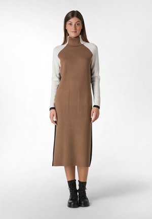 Knit dress in brown with a high neckline, long white sleeves, two front pockets, side slit, and paired with black lace-up boots.