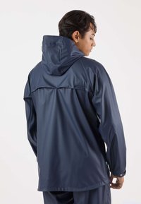 Marineblauwe waterdichte jas met capuchon, met een gladde, glanzende textuur, drukknopen en een losse pasvorm, gezien vanaf de achterkant.
