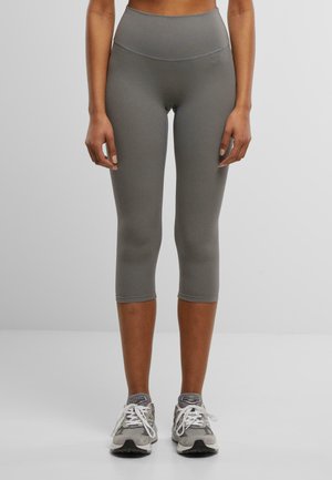 Grå capri leggings med høy midje og glatt tekstur, iført med grå treningssko og synlige lisser.