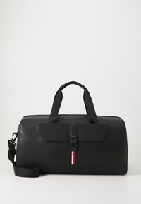 Black travel bag made of textured material, featuring dual top handles, an adjustable strap, and a front flap with a buckle. Red and white accent stripe.