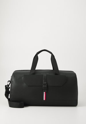 Zwarte reistas van getextureerd materiaal, met dubbele handvatten bovenaan, een verstelbare schouderband en een flap aan de voorkant met een gesp. Rood-witte accentstreep.