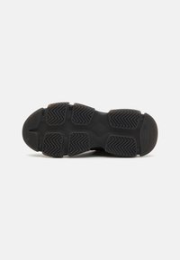 Suela de zapato deportivo negro con patrones de agarre texturizados, bordes redondeados y una estructura sólida que presenta múltiples segmentos de goma para tracción.