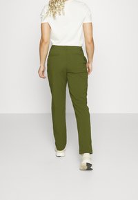 Gröna tapered byxor med en slät tygfinish, med två bakfickor, bärs med en vit t-shirt och ljusa sneakers.