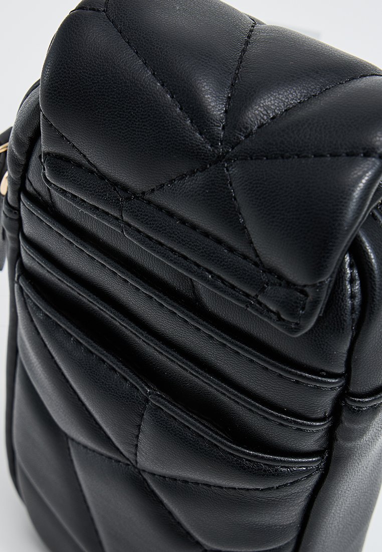 Primo piano di una borsa imbottita in pelle nera trapuntata con cuciture dettagliate e una zip in metallo dorato.