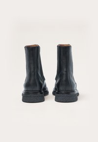 Botas de cuero negras hasta el tobillo con un acabado suave, suela de goma texturizada y tacón ligeramente elevado, con costuras verticales y un diseño elegante.