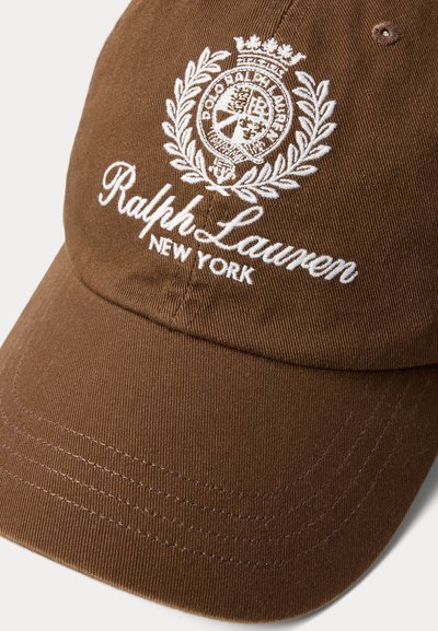 Καφέ βαμβακερό καπέλο μπέιζμπολ με κεντημένο λευκό λογότυπο και κείμενο που γράφει "Ralph Lauren New York." Διαθέτει δομημένη γείσο και υφή υφάσματος.