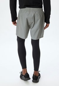 Lys grå træningsshorts med elastisk talje, parret med sorte leggings og sorte sneakers. Glat, let stofstruktur.