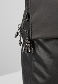 Sac à dos en tissu noir avec une surface texturée, équipé d'une fermeture éclair et d'un porte-clés avec une petite figurine noire attachée.