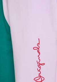 Light purple sweatshirt featuring red embroidered text and a green garment partially visible on the left side. Soft fabric texture.