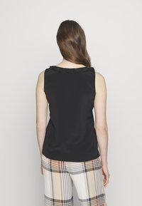 Top nero senza maniche con scollo arricciato, abbinato a pantaloni a quadri con motivi beige, marrone e blu.