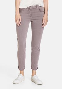 Jeans de longitud al tobillo en un tono malva claro con un ajuste slim, bolsillos frontales y detalles sutiles en el dobladillo, combinados con zapatillas blancas.