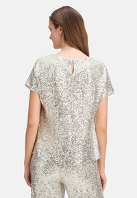 Zilveren pailletten top met korte mouwen, ronde halslijn en sleufdetail op de rug. Gladde textuur en glanzend oppervlak.
