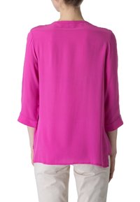 Blouse ample en rose vif, fabriquée en tissu léger. Elle présente des manches trois-quarts et un col rond avec un drapé doux.