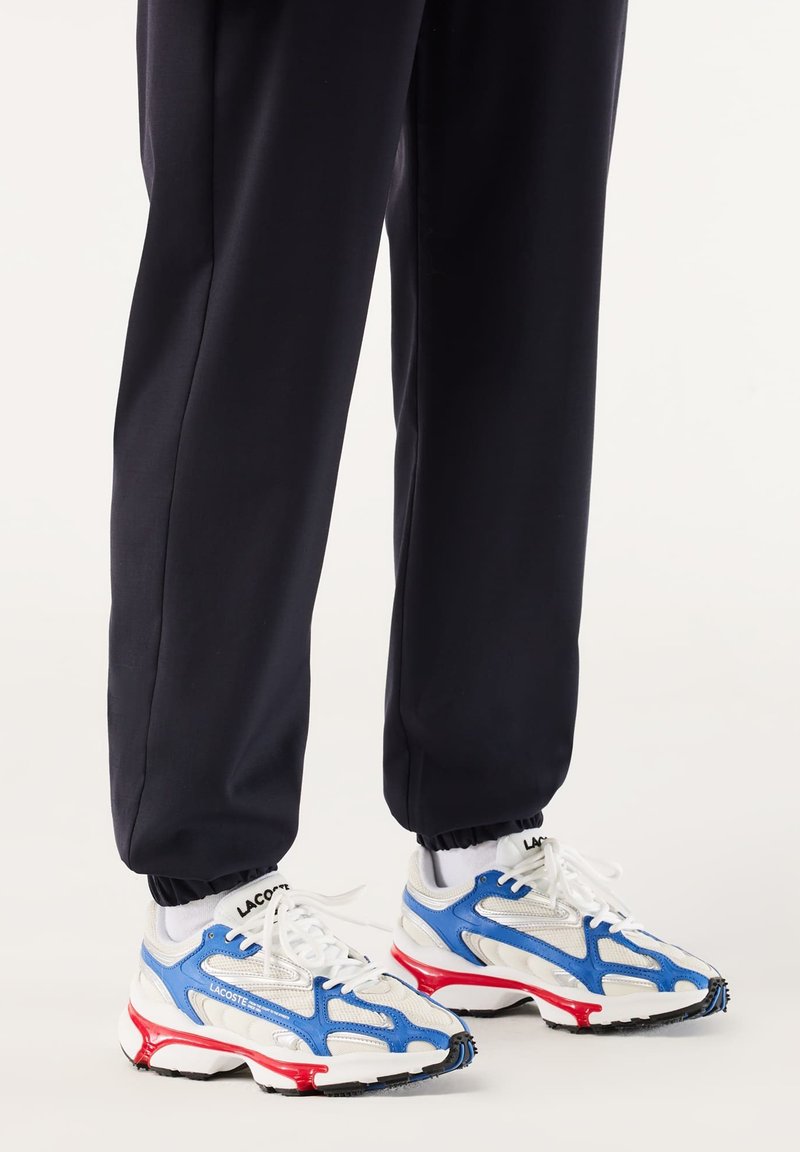 Baskets de course Lacoste avec une tige en mesh blanche ornée d'accents bleus et rouges, bout rond et semelle en caoutchouc épaisse avec un motif de traction texturé.