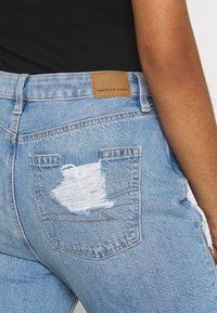 Jean en denim bleu clair avec un détail usé sur la poche. Présente un patch en cuir avec la marque "American Eagle" sur la taille arrière.