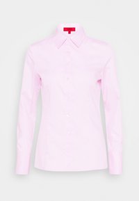Camicia da donna aderente di colore rosa chiaro, con maniche lunghe, colletto a punta e etichetta rossa all'interno del collo.