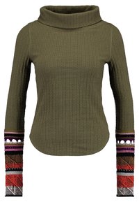 Olivgrön ribbad polotröja med långa ärmar som har flerfärgade geometriska stickade mönster och utskärningar nära handlederna.