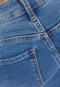 Blå denimtyg med synliga sömmar, en bältesögla och den övre kanten av en bakficka.