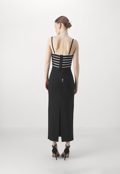 Abito nero aderente con righe bianche orizzontali sul corpetto. Presenta una zip sul retro e uno spacco alto fino alla coscia all'orlo, con spalline sottili.