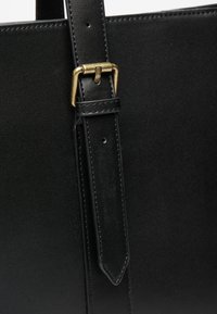 Black leather tote bag strap with a gold metal buckle. Smooth texture with reinforced stitching; adjustable length with multiple holes.