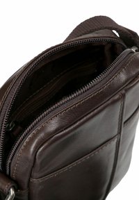 Bolso de hombro de piel marrón con una textura suave, que cuenta con un compartimento principal con cremallera y bolsillos externos. Acentos de herrajes duraderos.
