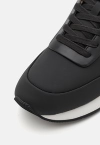 Musta spordijalats sileda, mati viimistlusega. Omab musti paelu ja kontrastset valget tallat. Minimalistlik kujundus.