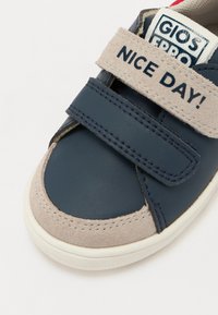 Baskets bleu marine avec tige en daim et cuir. Présentent une sangle Velcro avec le texte "JOURNÉE AGRÉABLE !", un col rembourré et une semelle en caoutchouc blanche.