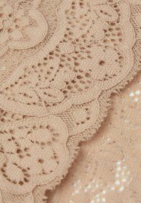 Beżowy materiał koronkowy z misternymi wzorami kwiatowymi i falbankami, ukazujący delikatną, teksturowaną powierzchnię z otwartymi splotami.