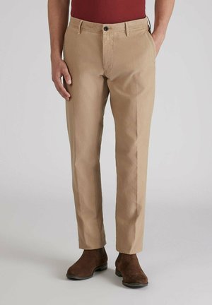 Chinos de algodón color beige con un diseño de pierna recta. Presentan bolsillos delanteros, pasadores para el cinturón y un cierre de botón. Combinados con botas de ante marrón.