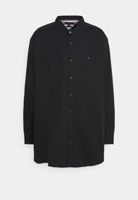 Camisa negra de manga larga con cuello abotonado, que presenta un pequeño logo en el pecho, hecha de tela lisa con un dobladillo recto.