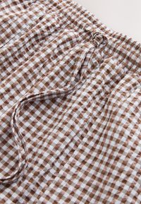 Ruda ir balta languota audinys su elastinga juosmens juosta ir raišteliu, pasižymintis minkšto medvilninio audinio raukšlėtu paviršiumi.