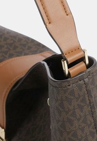 Borsa a mano in pelle marrone con motivo geometrico, dettagli in oro e tracolla color cuoio. Interno visibile, con rivestimento morbido e forma strutturata.