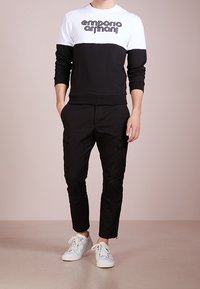 Black and white crewneck sweatshirt with "Emporio Armani" logo, paired with black tapered pants and white sneakers, featuring zippers.