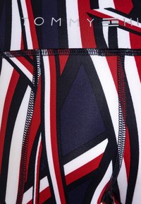 Miehekkäät miesten uimashortsit, joissa on punaisia, valkoisia ja laivastonsinisiä geometrisia kuvioita, näkyvillä saumoilla ja brändillä varustettu vyötärönauhatunnus.